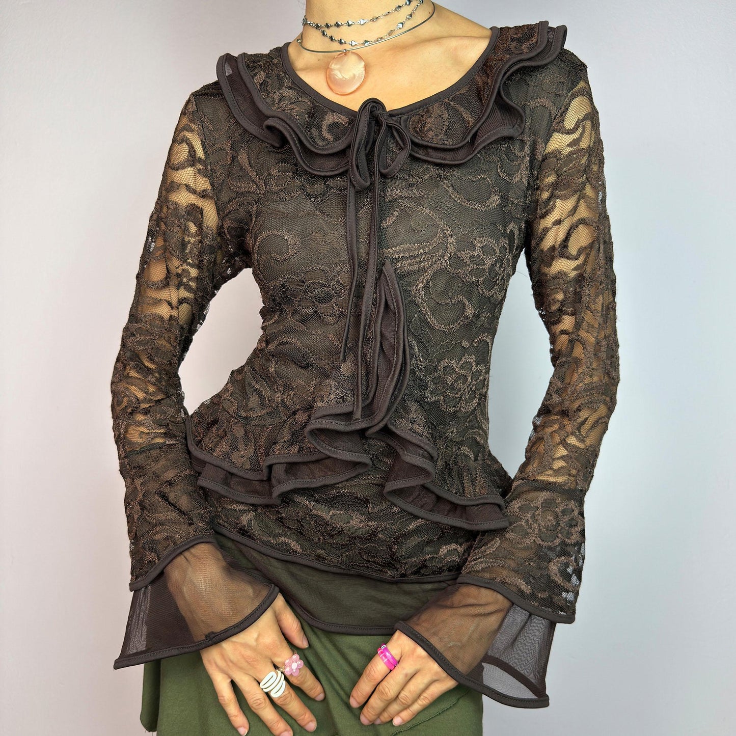 The Y2K Brown Lace Ruffle Top is a vintage 2000s statement piece, showcasing intricate floral lace throughout for a romantic and feminine look. This top features a stretchy semi-sheer fabric, layered ruffles along the neckline. adult world shop
