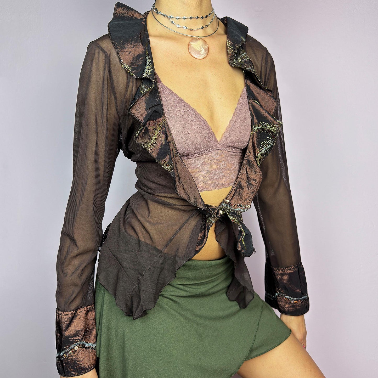 The Y2K Brown Mesh Tie Front Top is a vintage 2000s elegant and flirty piece. This semi-sheer mesh blouse features a tie-front closure and a cascade of ruffle detailing along the neckline and cuffs. adult world shop