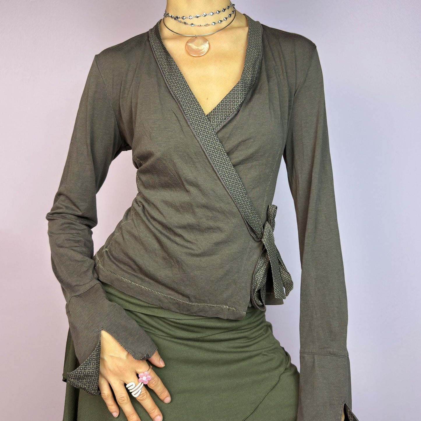 The Y2K Brown Wrap Cop Copine Top is a sleek and minimalist 2000s piece featuring a wrap-tie design with geometric-patterned trim details and flared cuffs. This top is crafted from a stretchy, comfortable fabric. adult world shop