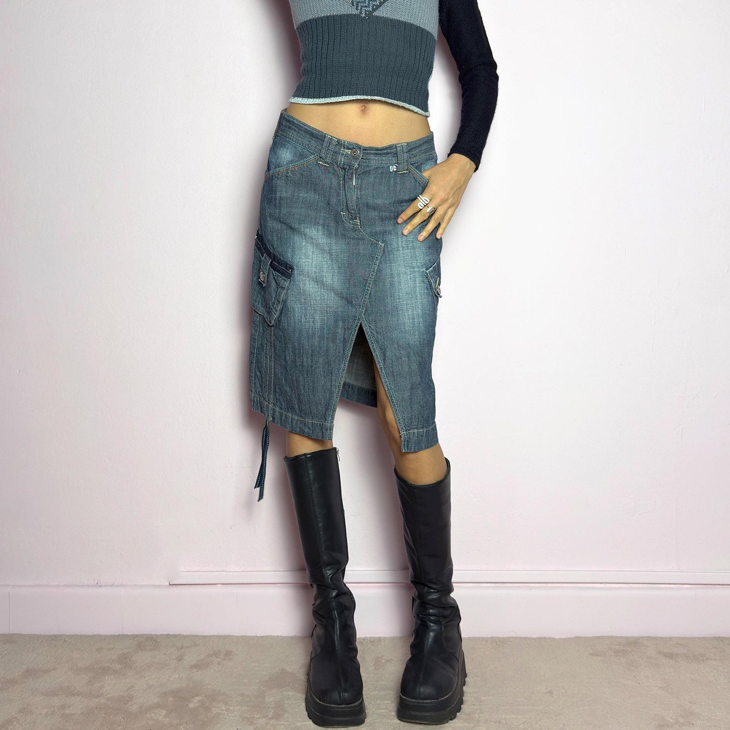The Y2K Deconstructed Denim Midi Skirt is a vintage 2000s standout piece featuring a structured dark-wash denim fabric with contrast stitching. Designed with an asymmetrical front slit, utility-style cargo pockets, and adjustable drawstrings. Finished with a button and zipper closure, belt loops, and a mid-length silhouette, it's perfect for effortless grunge and utilitarian-inspired outfits. adult world shop