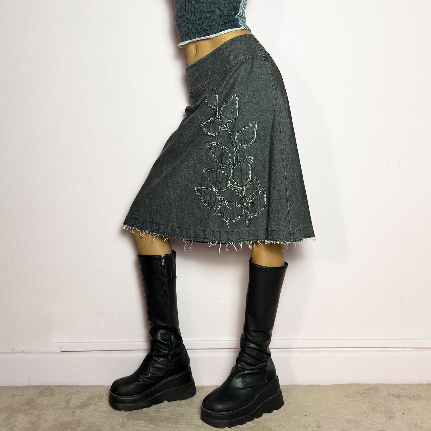 The Y2K Denim Gray Midi Skirt is a vintage 2000s piece featuring a faded gray wash, raw hem, and a unique floral sequin embroidery design. Crafted from structured denim, this skirt has an A-line silhouette that drapes effortlessly. Designed with a back zipper closure, the unfinished hem adds a deconstructed, edgy touch, making it perfect for casual outfits. adult world shop