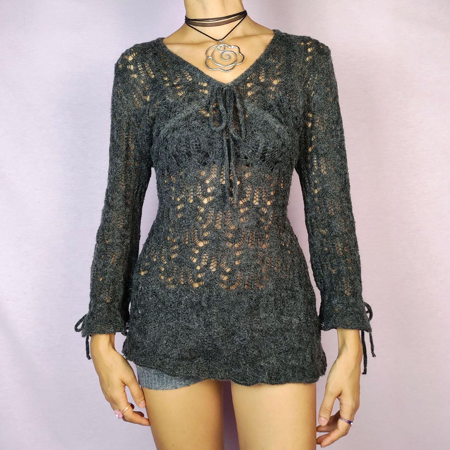 The Y2K Gray Sheer Sweater is a vintage 2000s pullover featuring a delicate knit pattern with semi-sheer details, offering a lightweight yet cozy feel. Designed with three quarter sleeves and a tie detail at the neckline, this sweater