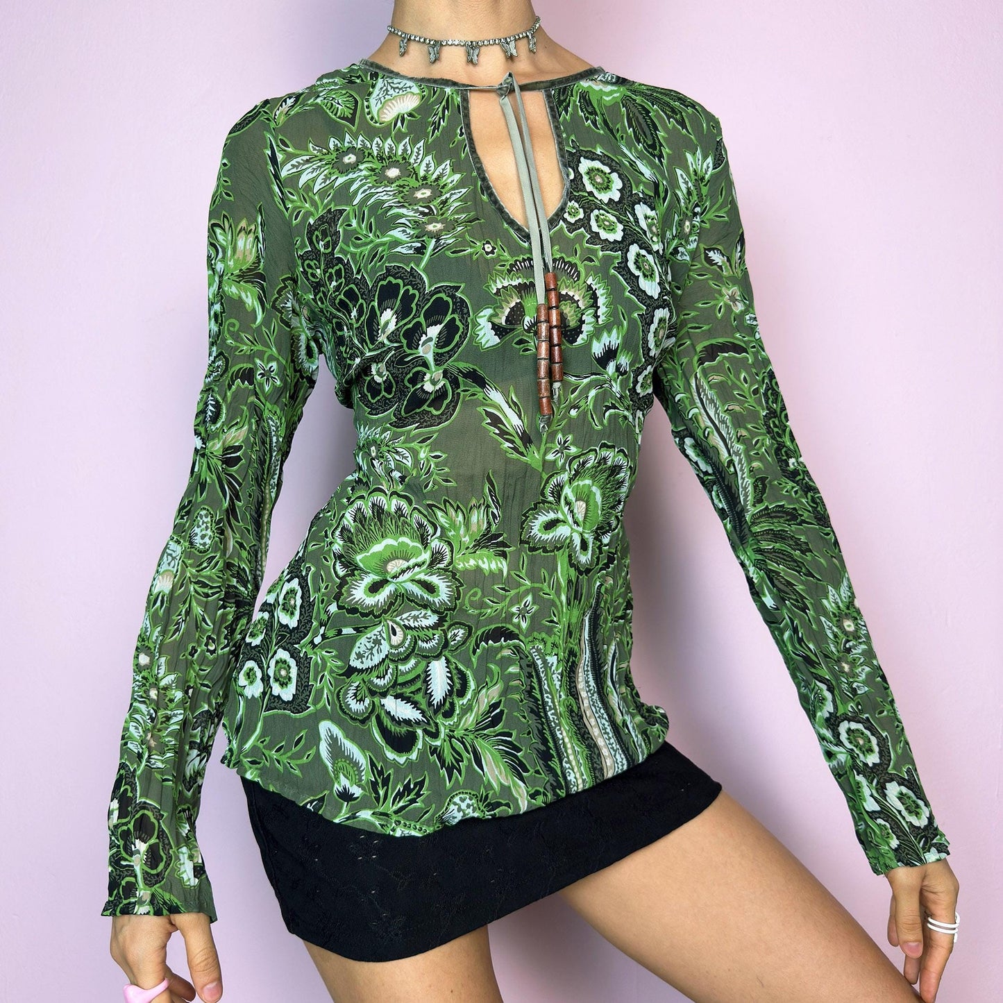The Y2K Green Boho Tie Front Top is a vintage 2000s piece featuring an abstract floral print on lightweight, semi-sheer fabric. Designed with a front keyhole neckline and adjustable tie adorned with wooden bead details. The long sleeves and breathable material make it comfy and flattering. A unique top perfect for summer layering, festival outfits, fairy grunge, or earthy boho styles.