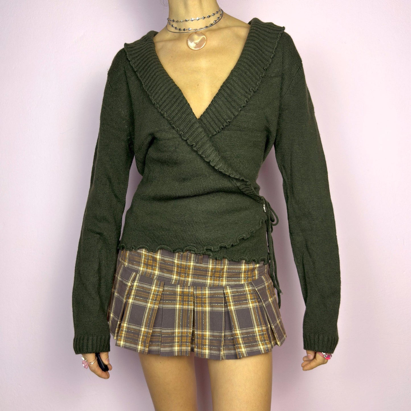 The Y2K Green Wrap Tie Cardigan is a vintage 2000s piece, featuring a deep V-neck, wrap-front design with tie closure, and subtle ruffle details along the neckline. Made from a soft mohair and acrylic blend, this cardigan has a rich forest green tone, perfect for layering over casual or dressed-up outfits. adult world shop