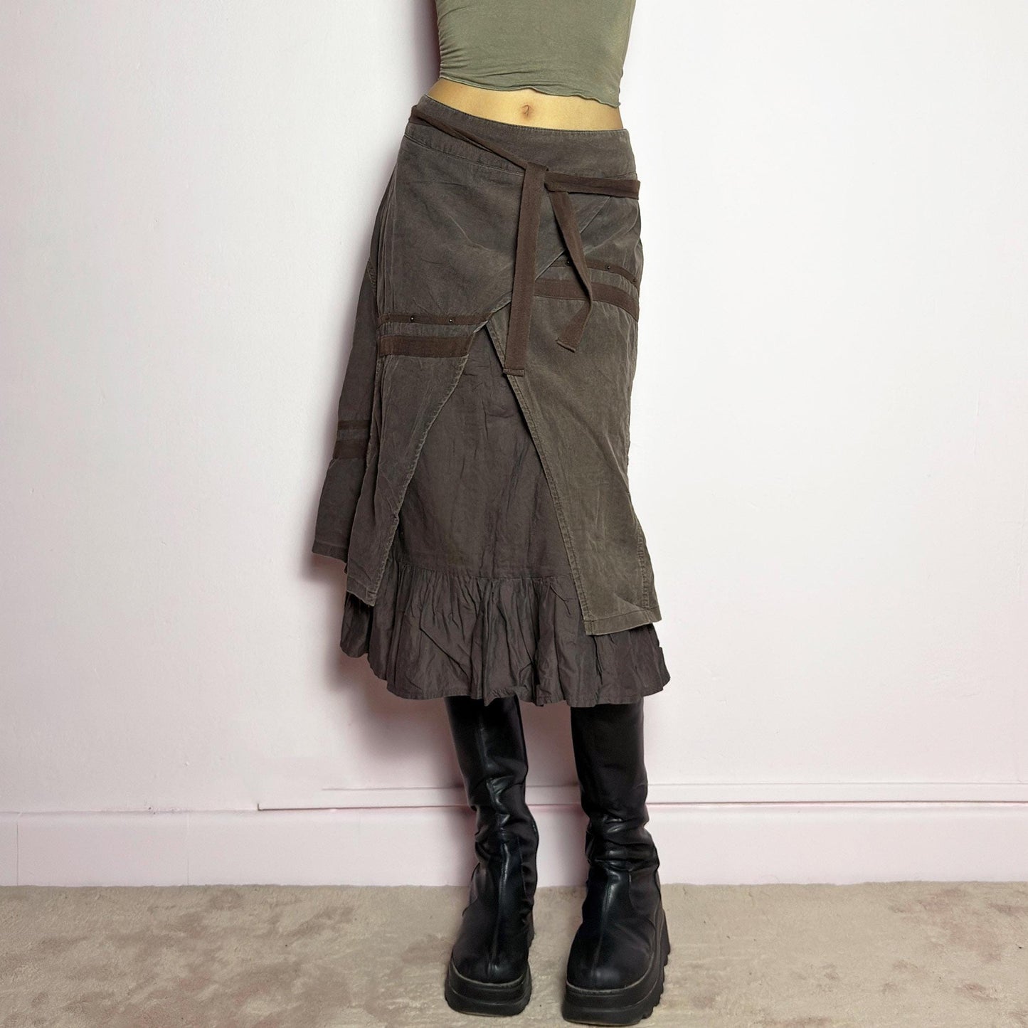 The Y2K Layered Brown Midi Skirt is a unique vintage 2000s piece featuring an asymmetric wrap design with a layered ruffle hem. Made from corduroy-cotton fabric, it includes tie closures for an adjustable fit, a back zipper closure, and subtle stitched detailing that adds a deconstructed touch. Perfect for earthy, bohemian, or avant-garde styling. adult world shop