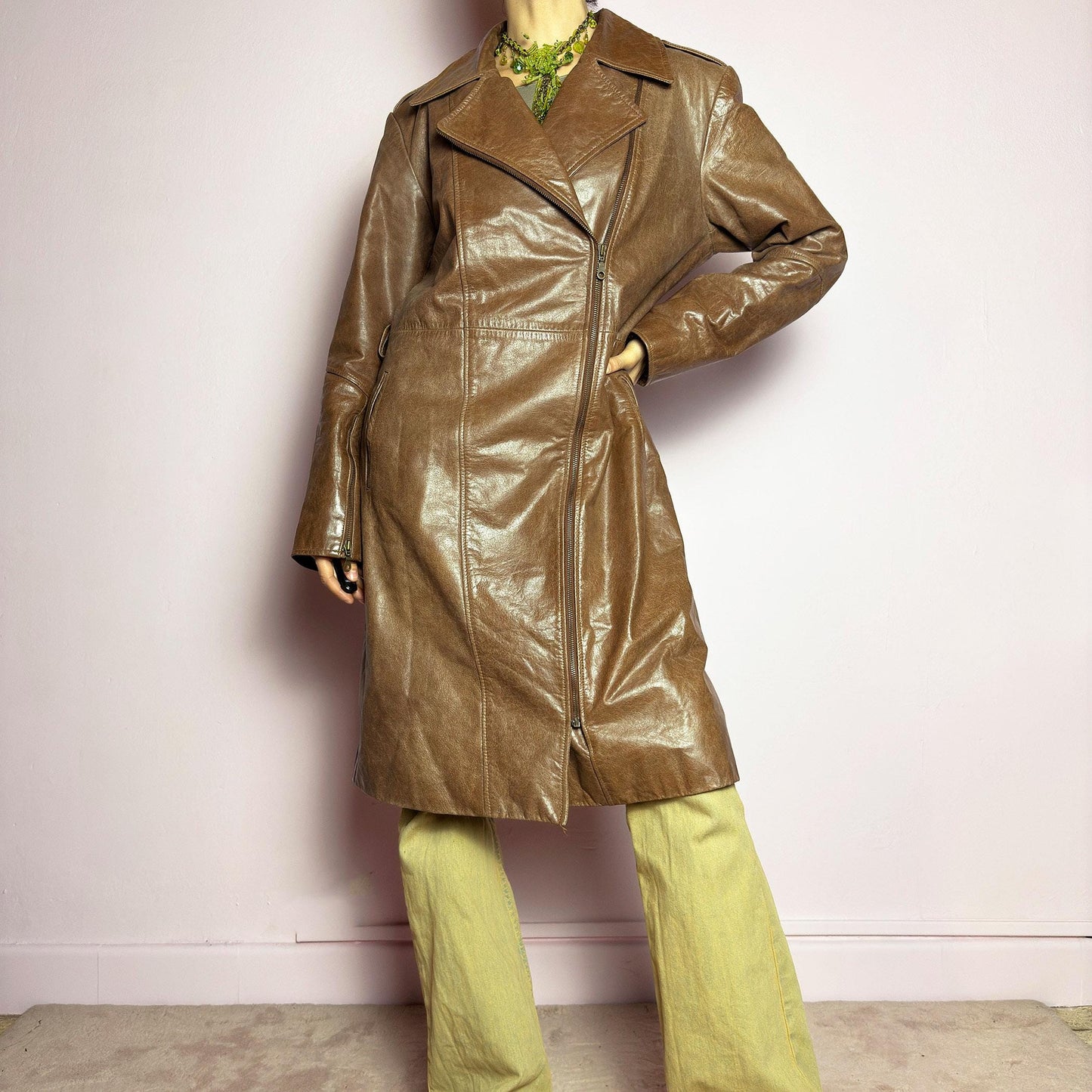 The Y2K Long Brown Leather Coat is a heavy, structured vintage 2000s piece crafted from genuine leather. It features an asymmetrical zip closure, a wide lapel collar, and a belted waist for a cinched silhouette. The coat includes pockets and a smooth lining for comfort. With its durable construction and timeless design, this vintage long leather coat is perfect for edgy streetwear or sophisticated layering. adult world shop