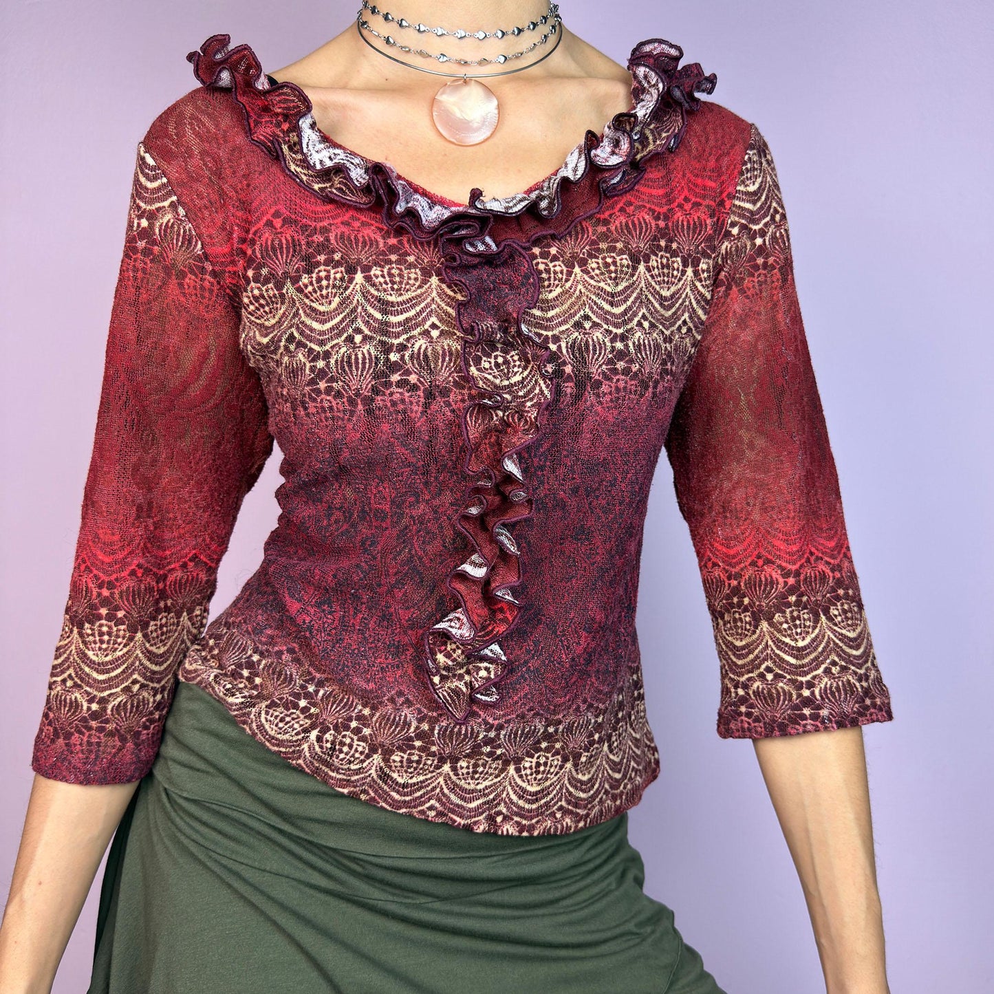The Y2K Maroon Ruffle Mesh Top is a romantic vintage 2000s piece. Featuring a semi-sheer lace-inspired design in warm red tones, it showcases intricate patterns complemented by a ruffled neckline and 3/4 sleeves. adult world shop