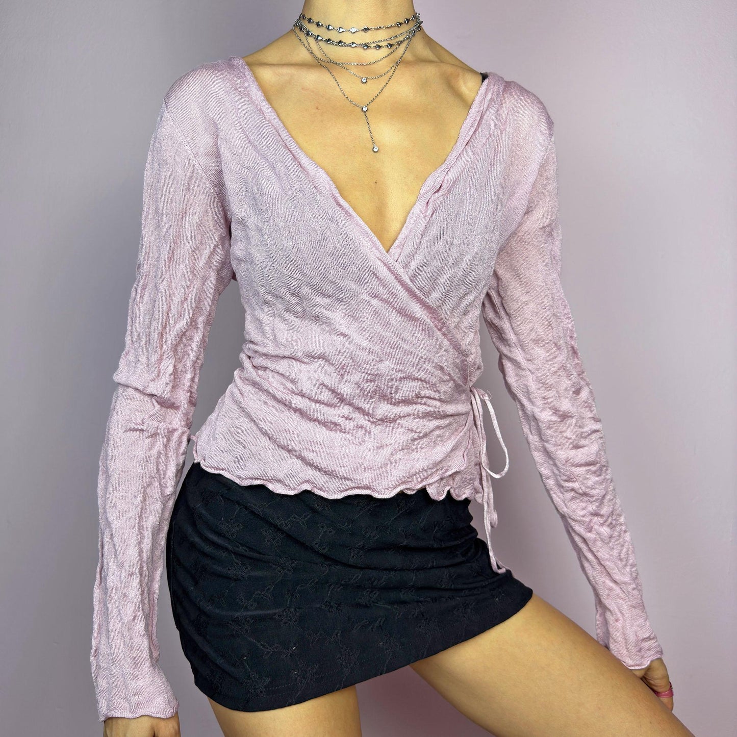 The Y2K Pink Wrap Tie Cardigan is a vintage 2000s delicate and feminine piece featuring a light pink hue and a textured knit fabric. Its wrap-around design ties at the side, creating an adjustable and flattering fit. adult world shop