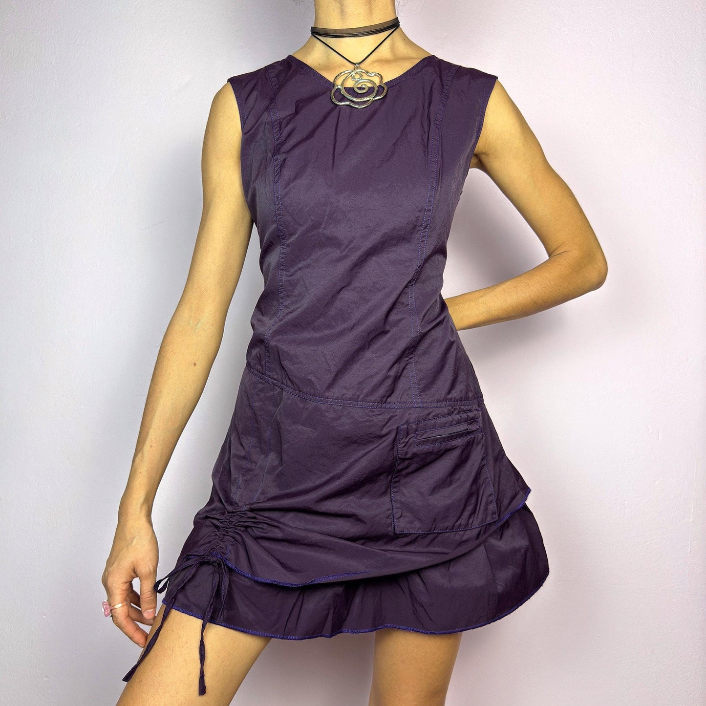 The Y2K Purple Layered Mini Dress is a vintage 2000s sleeveless dress in a deep purple hue, featuring a structured, layered silhouette, a side pocket, an adjustable drawstring ruched detail on the side for a customizable fit. adult world shop