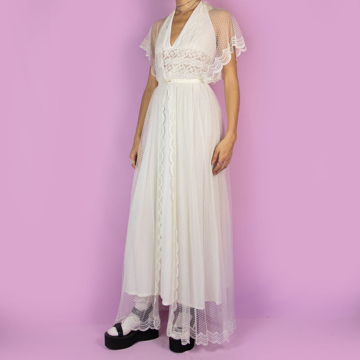 The Vintage 90s White Sheer Duster is a dreamy and ethereal robe, featuring a sheer polka-dot overlay with delicate lace detailing along the edges. The flowy silhouette, flutter sleeves, and maxi length add a romantic charm. Adult World Shop