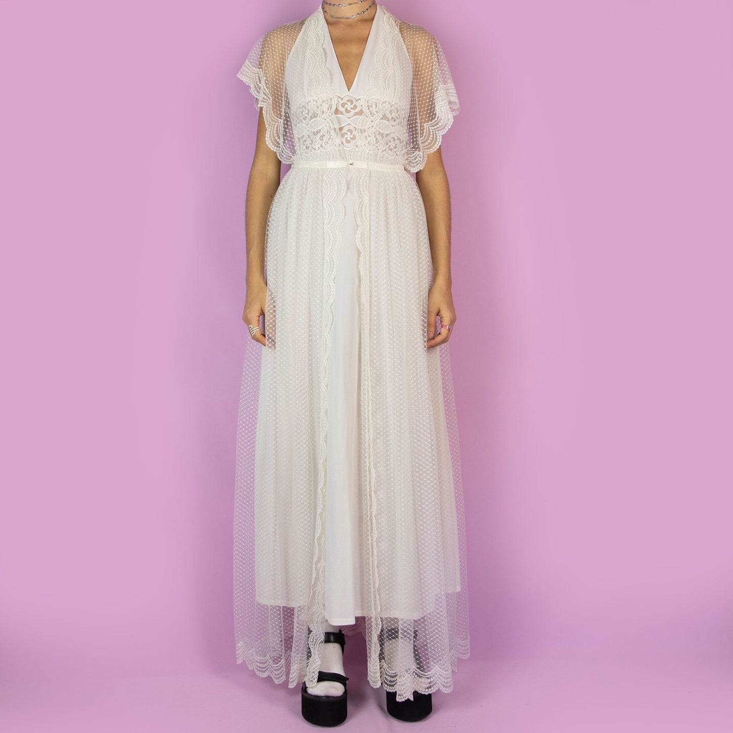 The Vintage 90s White Sheer Duster is a dreamy and ethereal robe, featuring a sheer polka-dot overlay with delicate lace detailing along the edges. The flowy silhouette, flutter sleeves, and maxi length add a romantic charm. Adult World Shop