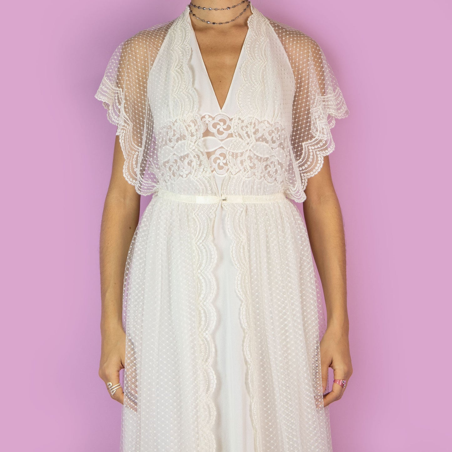 The Vintage 90s White Sheer Duster is a dreamy and ethereal robe, featuring a sheer polka-dot overlay with delicate lace detailing along the edges. The flowy silhouette, flutter sleeves, and maxi length add a romantic charm. Adult World Shop