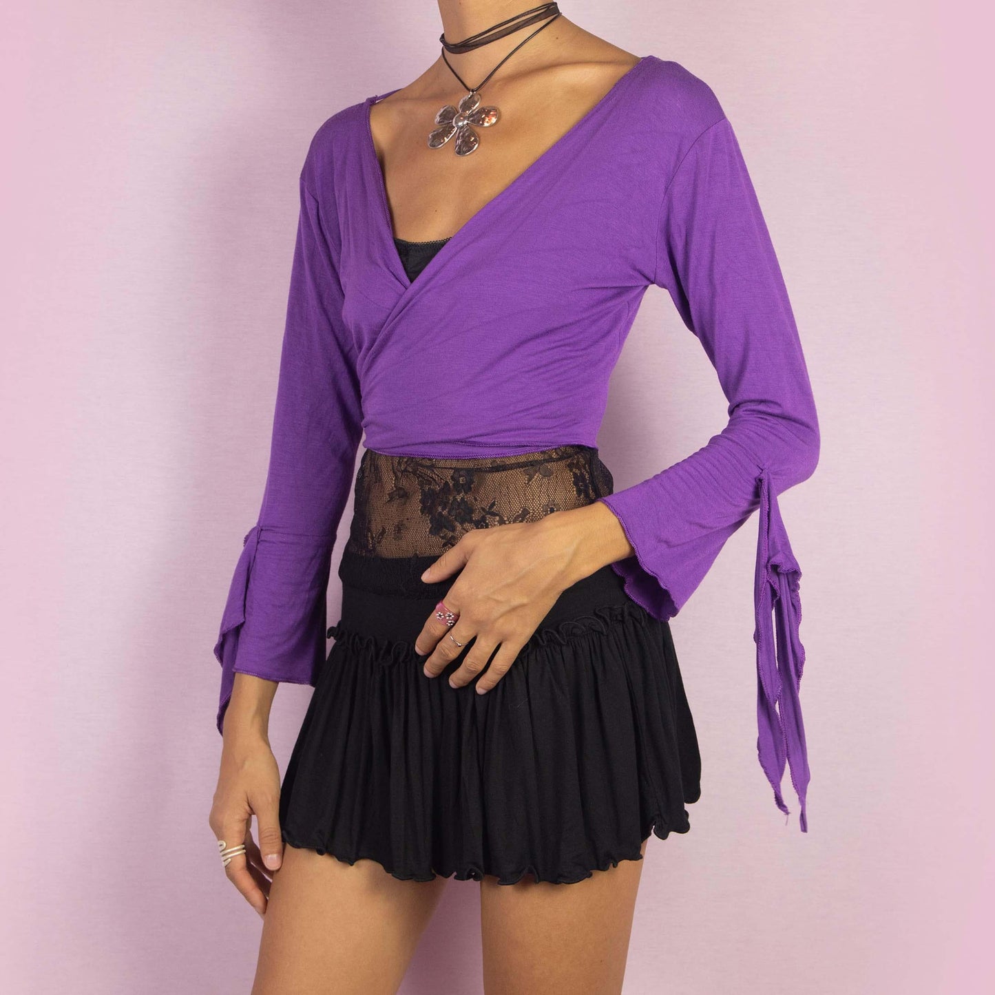 The Y2K Purple Tie Bolero is a vintage 2000s cropped cardigan featuring a vibrant purple color, front tie closure, and unique bell sleeves. The open-back design with criss-cross straps adds a playful touch