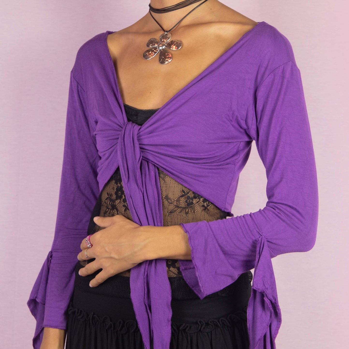 The Y2K Purple Tie Bolero is a vintage 2000s cropped cardigan featuring a vibrant purple color, front tie closure, and unique bell sleeves. The open-back design with criss-cross straps adds a playful touch