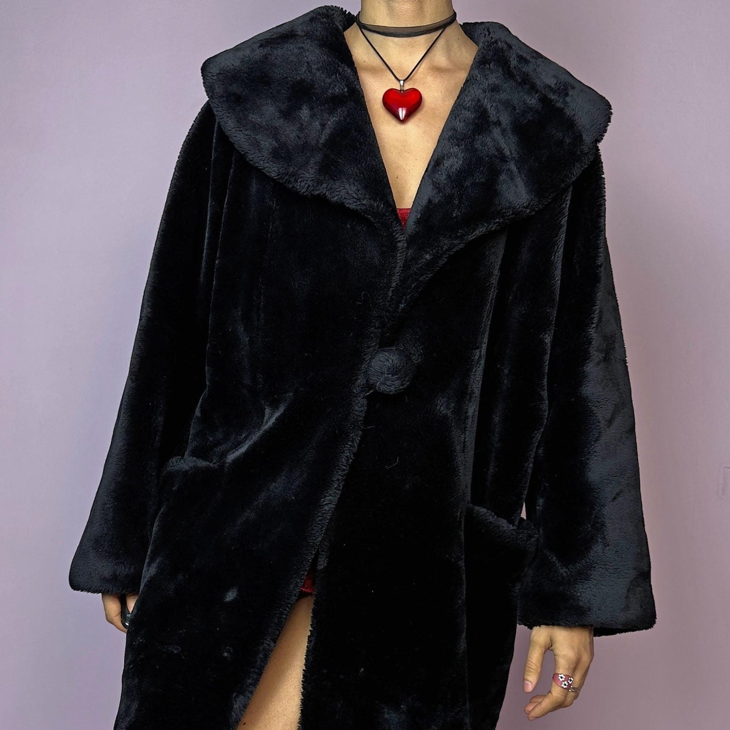 The Vintage 90s Black Faux Fur Coat showcases a faux fur material for a sophisticated and cozy winter style. It features a plush oversized collar, a chic fabric-covered button closure, and pockets. Perfect for winter outings or evening events.