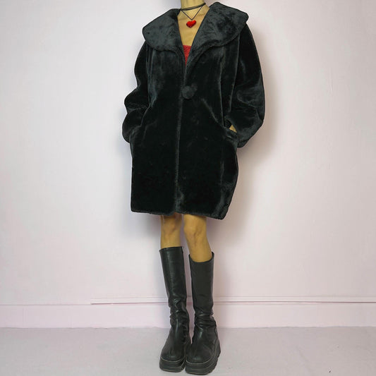 The Vintage 90s Black Faux Fur Coat showcases a faux fur material for a sophisticated and cozy winter style. It features a plush oversized collar, a chic fabric-covered button closure, and pockets. Perfect for winter outings or evening events.