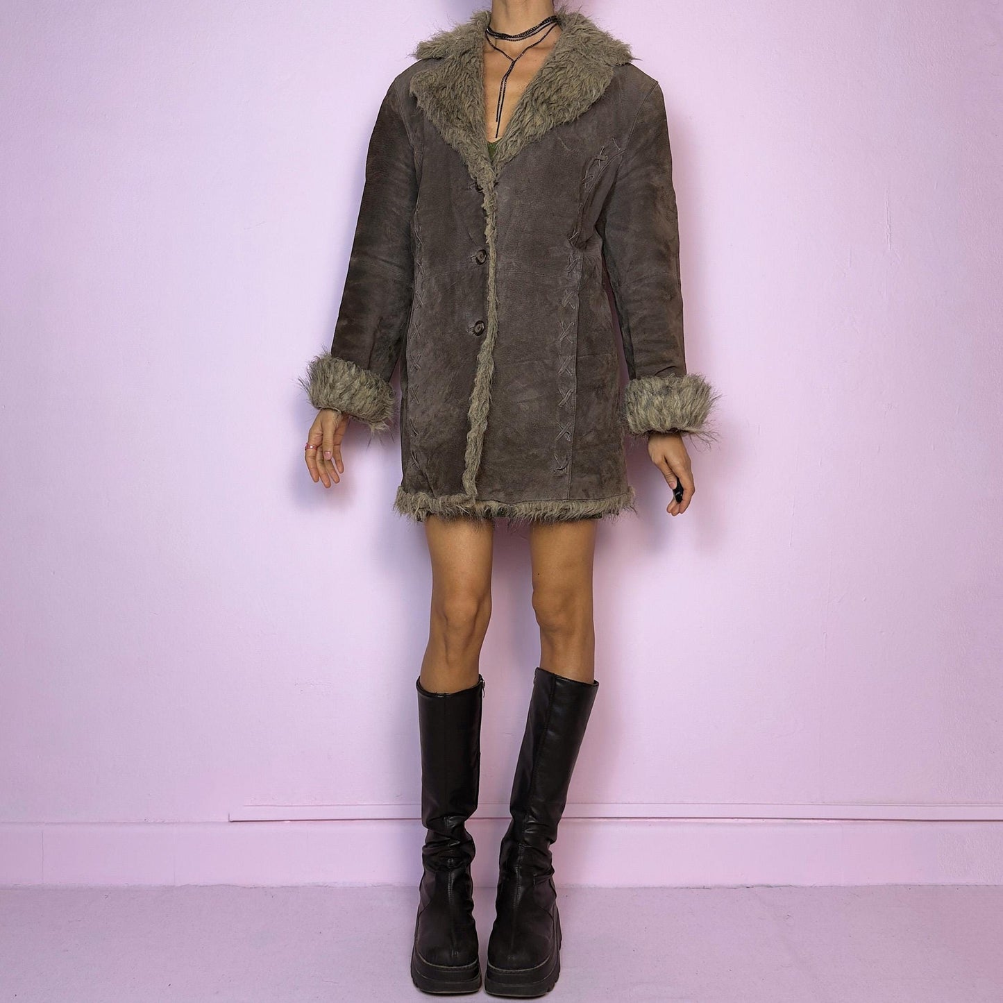 The Vintage 90s Brown Suede Penny Lane Coat showcases a brown leather suede finish paired with soft faux fur trims along the collar, cuffs, and hemline. This jacket features button closures and intricate stitch details. Its timeless design