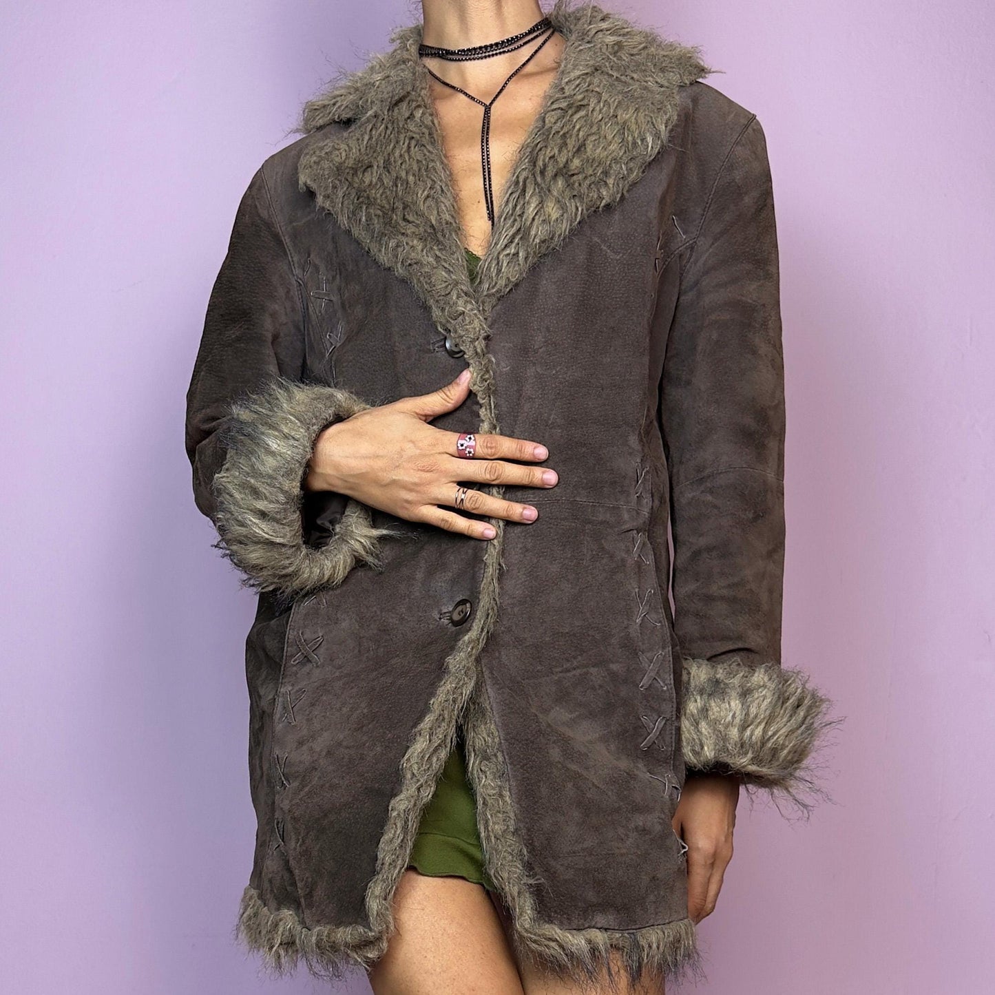 The Vintage 90s Brown Suede Penny Lane Coat showcases a brown leather suede finish paired with soft faux fur trims along the collar, cuffs, and hemline. This jacket features button closures and intricate stitch details. Its timeless design