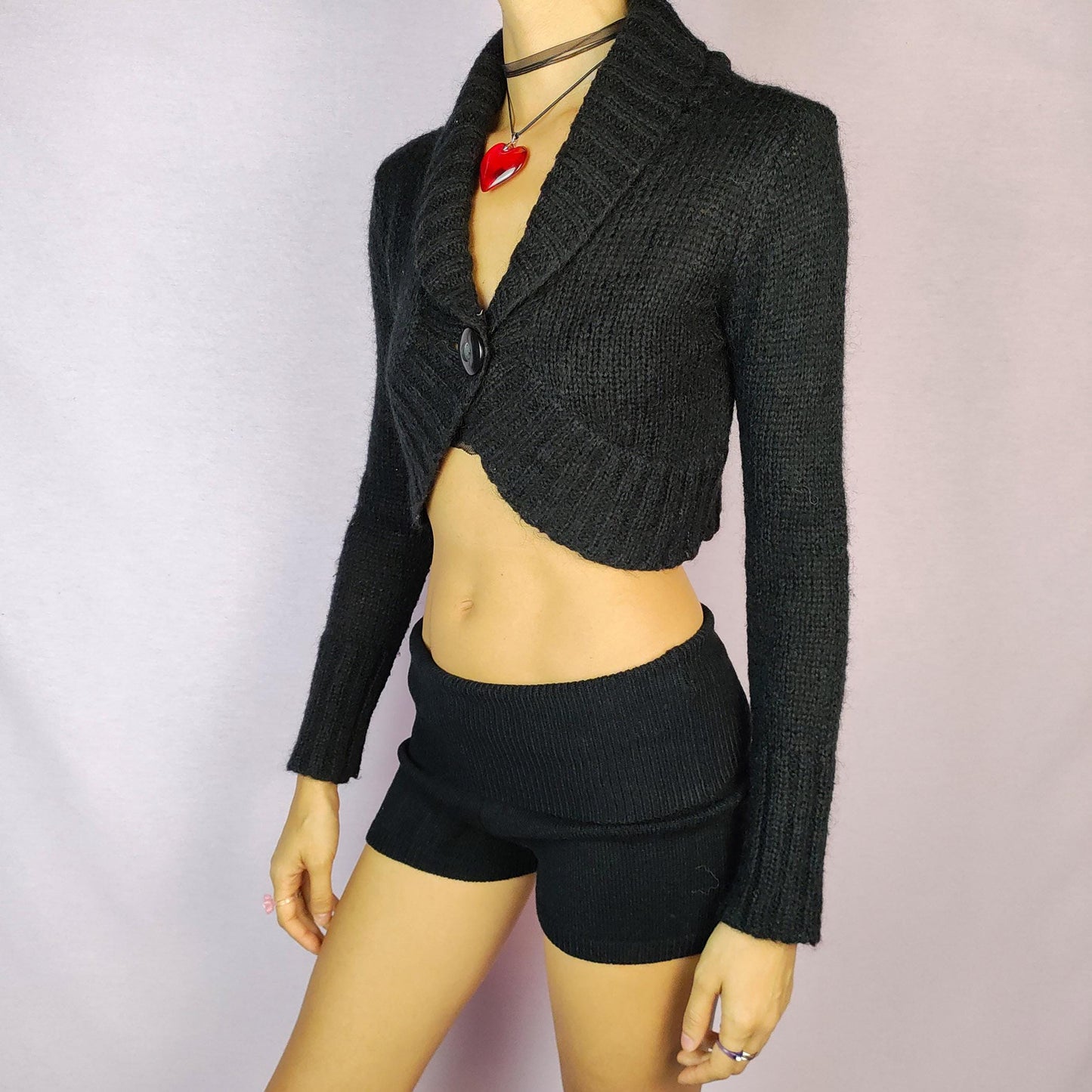 The Y2K Black Cropped Bolero Cardigan is a vintage 2000s piece featuring a chic single-button front closure and a shawl collar. This bolero-style cardigan is crafted from a soft knit fabric and the cropped silhouette makes it perfect for layering.