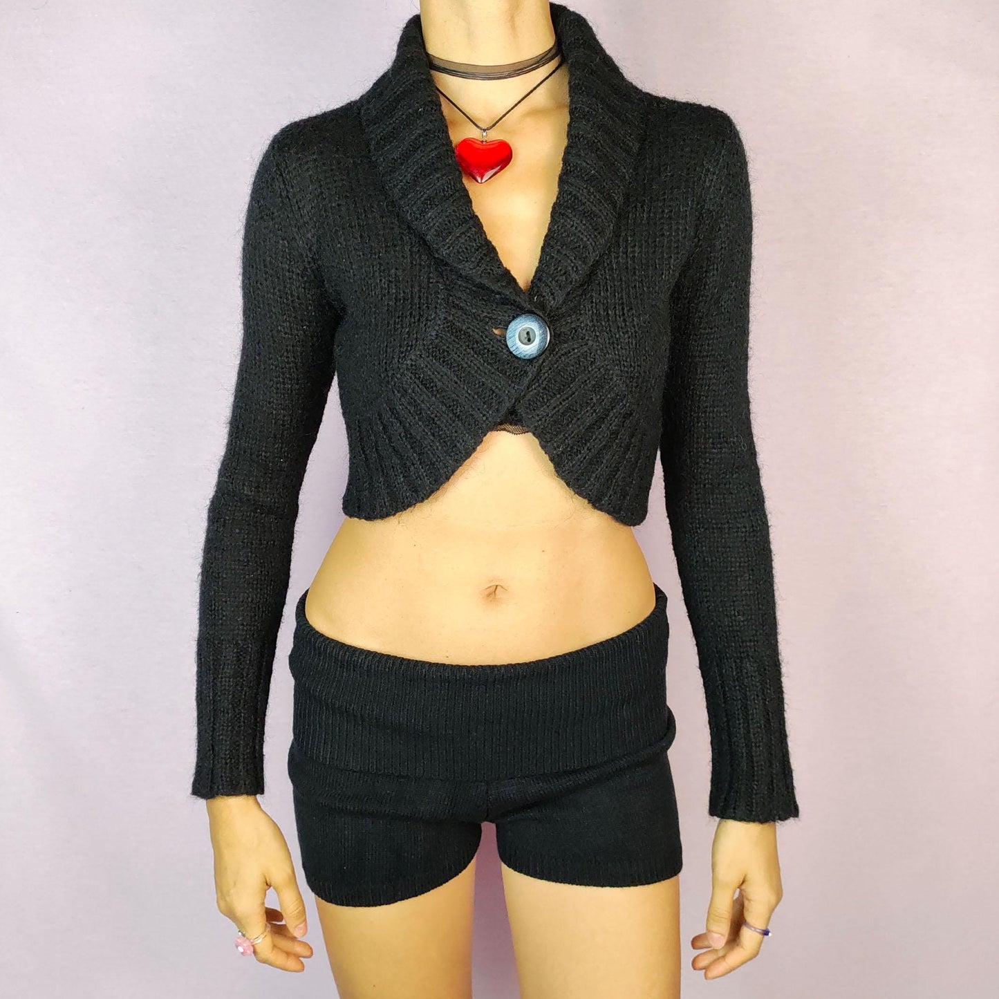 The Y2K Black Cropped Bolero Cardigan is a vintage 2000s piece featuring a chic single-button front closure and a shawl collar. This bolero-style cardigan is crafted from a soft knit fabric and the cropped silhouette makes it perfect for layering.
