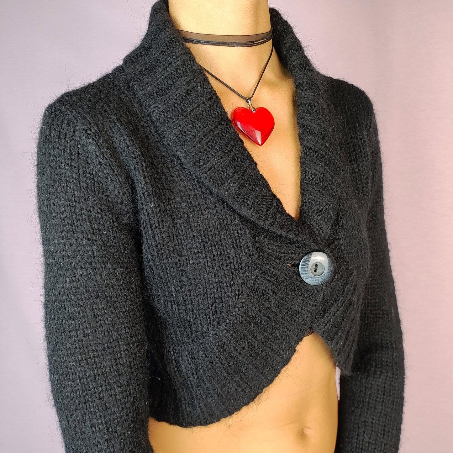 The Y2K Black Cropped Bolero Cardigan is a vintage 2000s piece featuring a chic single-button front closure and a shawl collar. This bolero-style cardigan is crafted from a soft knit fabric and the cropped silhouette makes it perfect for layering.
