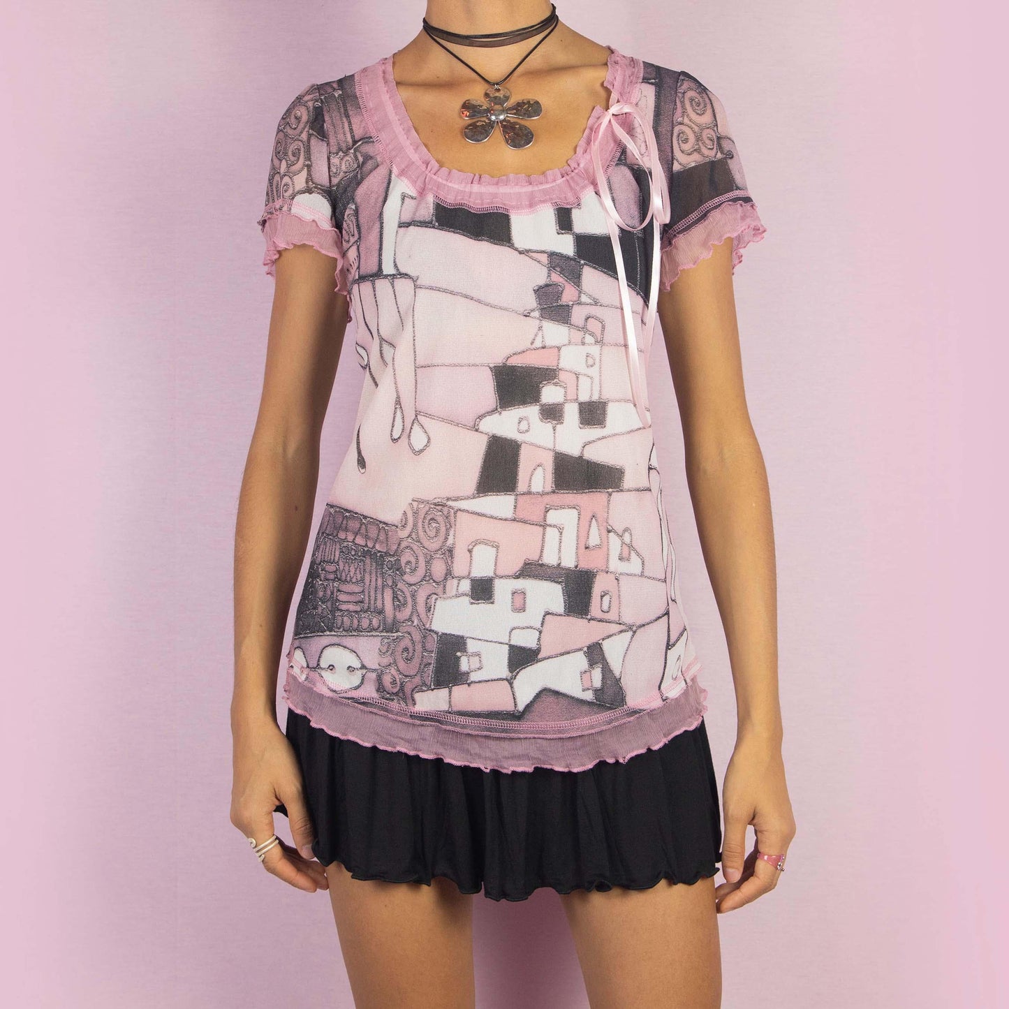 The Y2K Paint Mesh Tie Top is a vintage 2000s shirt featuring a semi-sheer fabric with a pink and black art painting-inspired print. Designed with ruffled edges, short sleeves, and a delicate side tie detail, this top is a whimsical choice