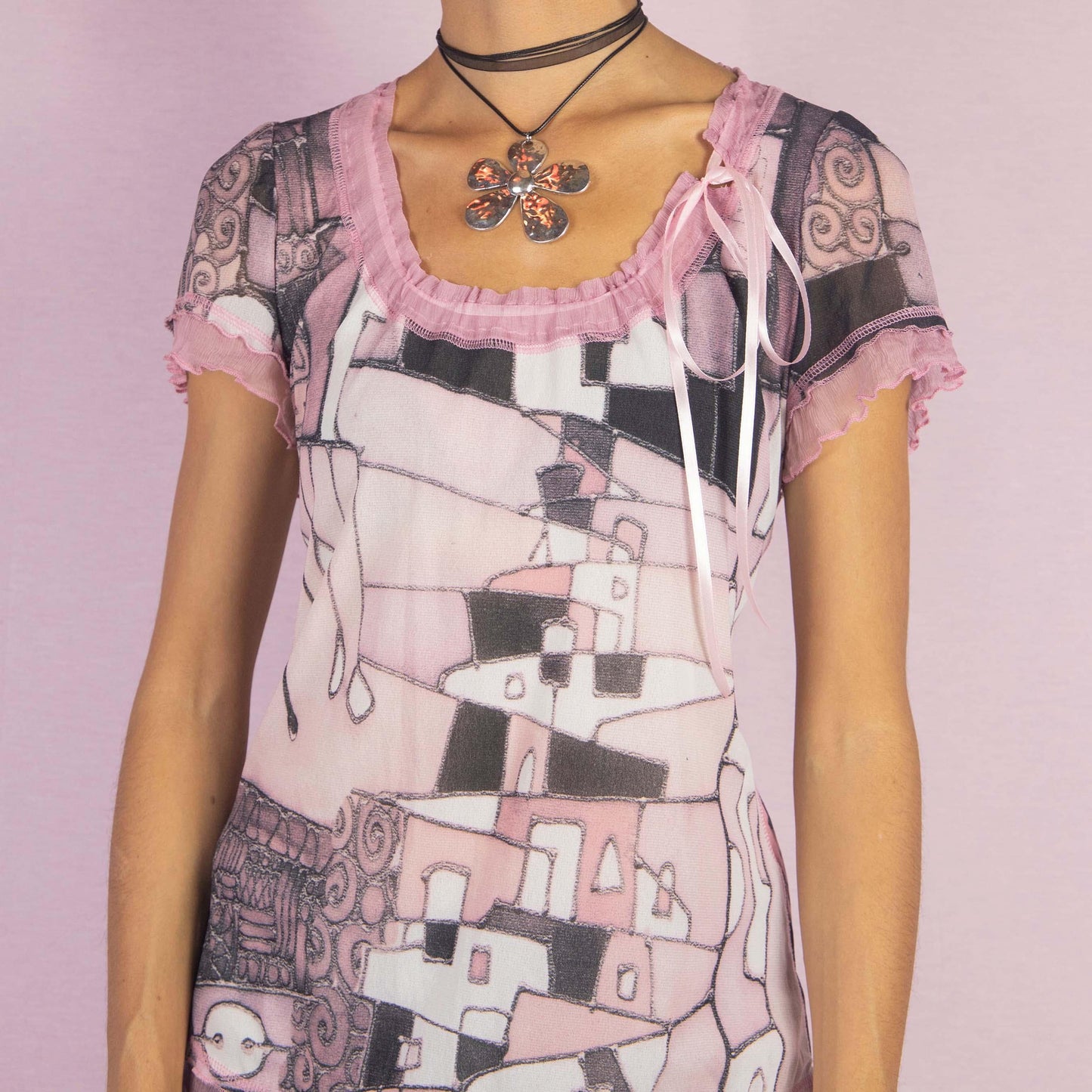 The Y2K Paint Mesh Tie Top is a vintage 2000s shirt featuring a semi-sheer fabric with a pink and black art painting-inspired print. Designed with ruffled edges, short sleeves, and a delicate side tie detail, this top is a whimsical choice
