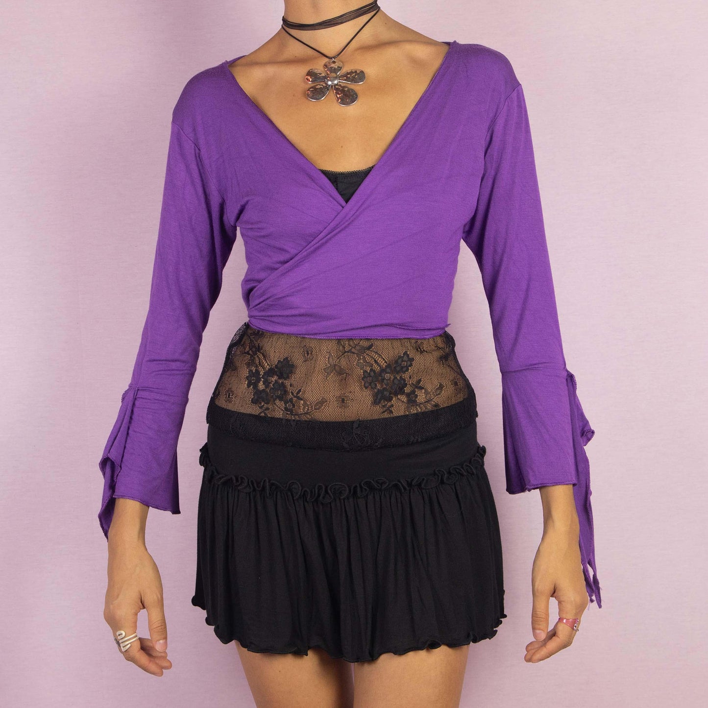 The Y2K Purple Tie Bolero is a vintage 2000s cropped cardigan featuring a vibrant purple color, front tie closure, and unique bell sleeves. The open-back design with criss-cross straps adds a playful touch