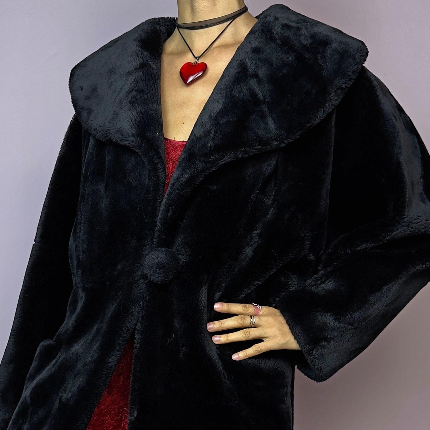 The Vintage 90s Black Faux Fur Coat showcases a faux fur material for a sophisticated and cozy winter style. It features a plush oversized collar, a chic fabric-covered button closure, and pockets. Perfect for winter outings or evening events.