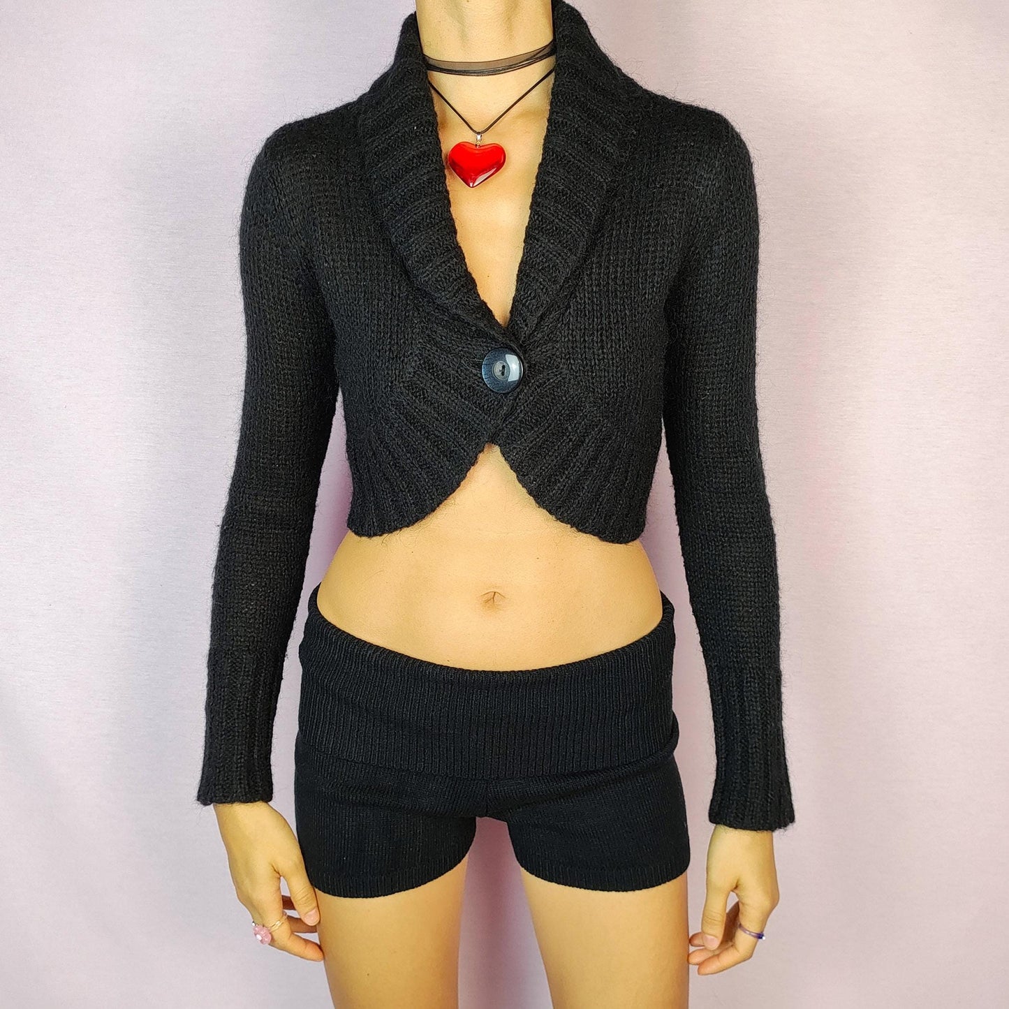 The Y2K Black Cropped Bolero Cardigan is a vintage 2000s piece featuring a chic single-button front closure and a shawl collar. This bolero-style cardigan is crafted from a soft knit fabric and the cropped silhouette makes it perfect for layering.