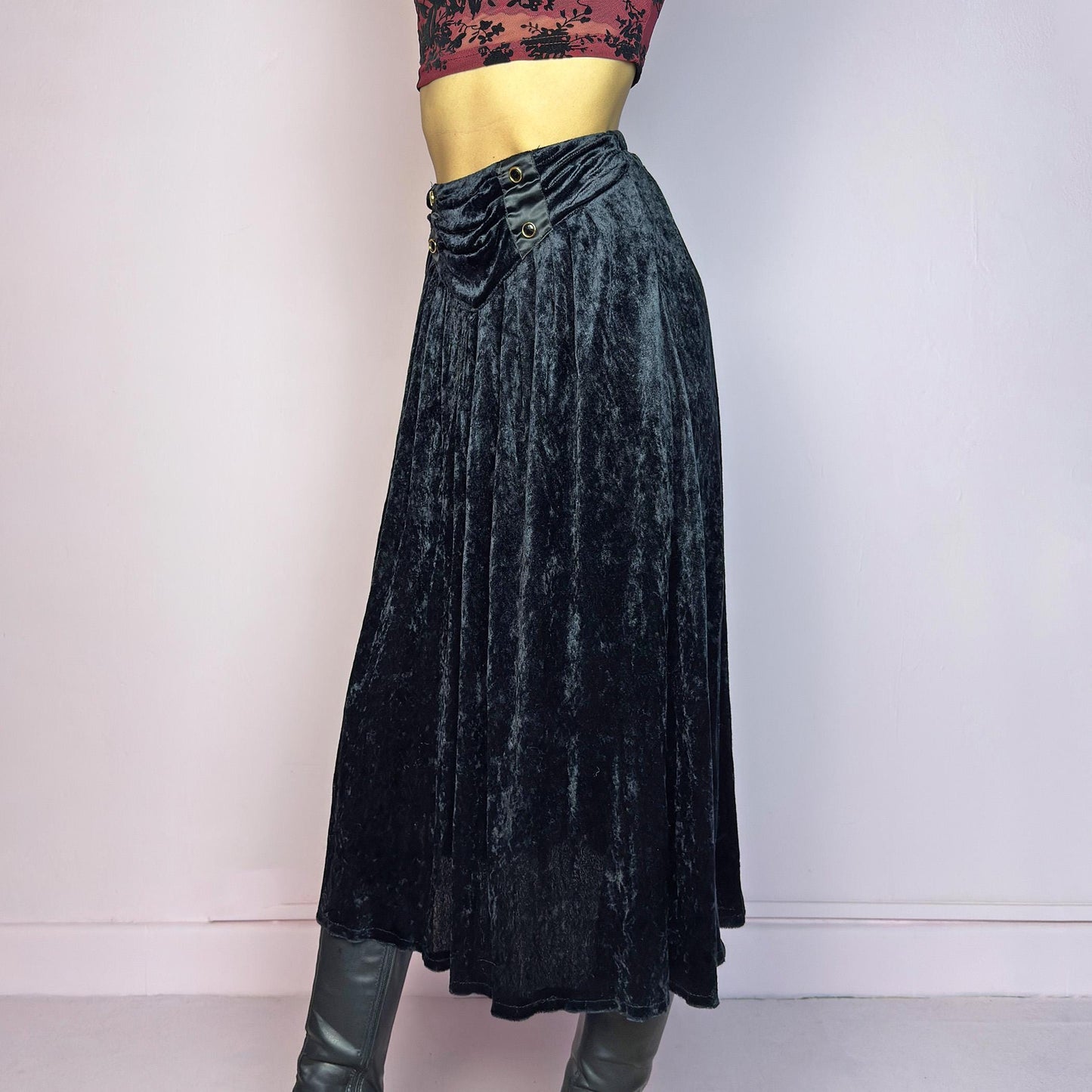 The Vintage 90s Black Velvet Midi Skirt is crafted from soft velvet and features an elastic waistband detail with button accents and a flowing A-line silhouette. Ideal for night parties and embodies a whimsical goth aesthetic. Adult World Shop