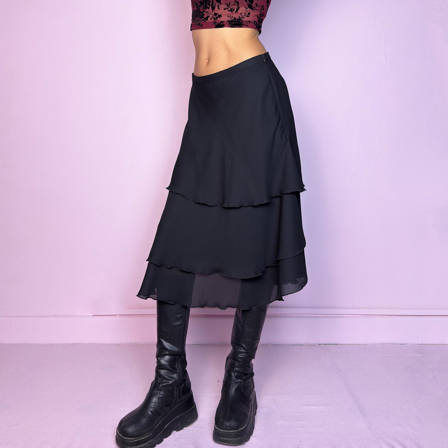 The Vintage 90s Black Layered Tiered Skirt features a flowy, tiered design with cascading chiffon-like layers. It includes a side zipper closure. Its versatile length and elegant style make it perfect for evening parties. Adult World Shop