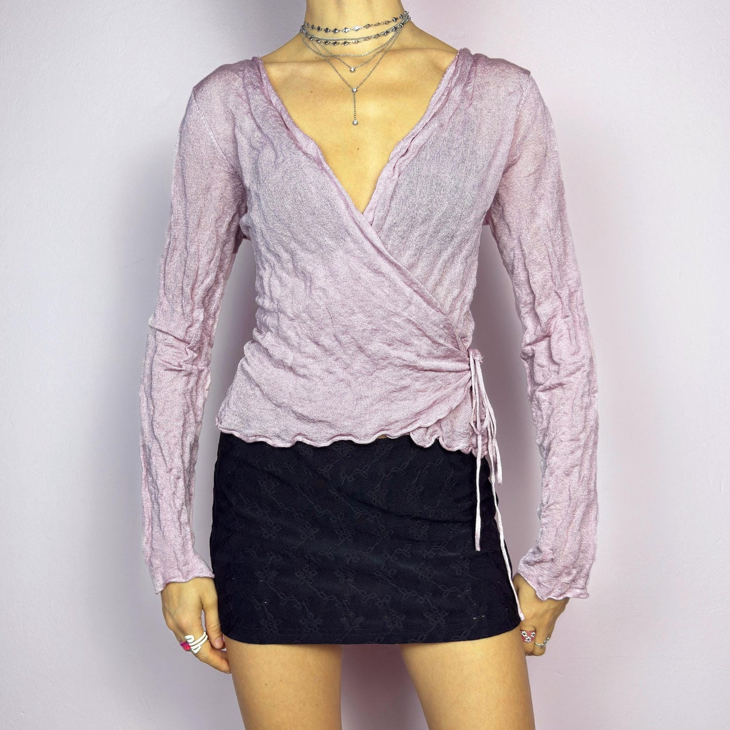 The Y2K Pink Wrap Tie Cardigan is a vintage 2000s delicate and feminine piece featuring a light pink hue and a textured knit fabric. Its wrap-around design ties at the side, creating an adjustable and flattering fit. adult world shop