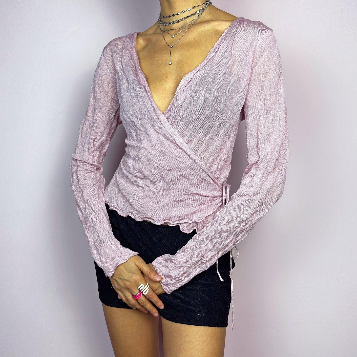 The Y2K Pink Wrap Tie Cardigan is a vintage 2000s delicate and feminine piece featuring a light pink hue and a textured knit fabric. Its wrap-around design ties at the side, creating an adjustable and flattering fit. adult world shop