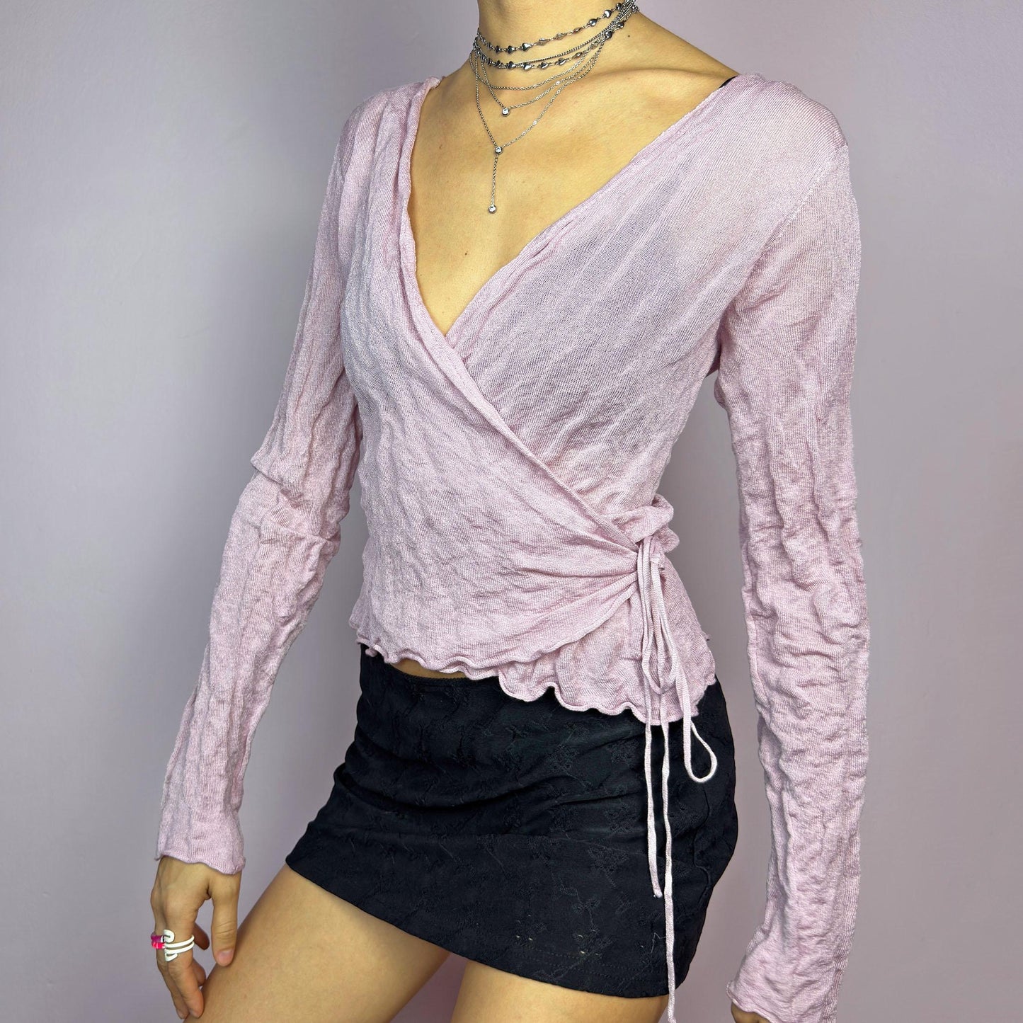 The Y2K Pink Wrap Tie Cardigan is a vintage 2000s delicate and feminine piece featuring a light pink hue and a textured knit fabric. Its wrap-around design ties at the side, creating an adjustable and flattering fit. adult world shop