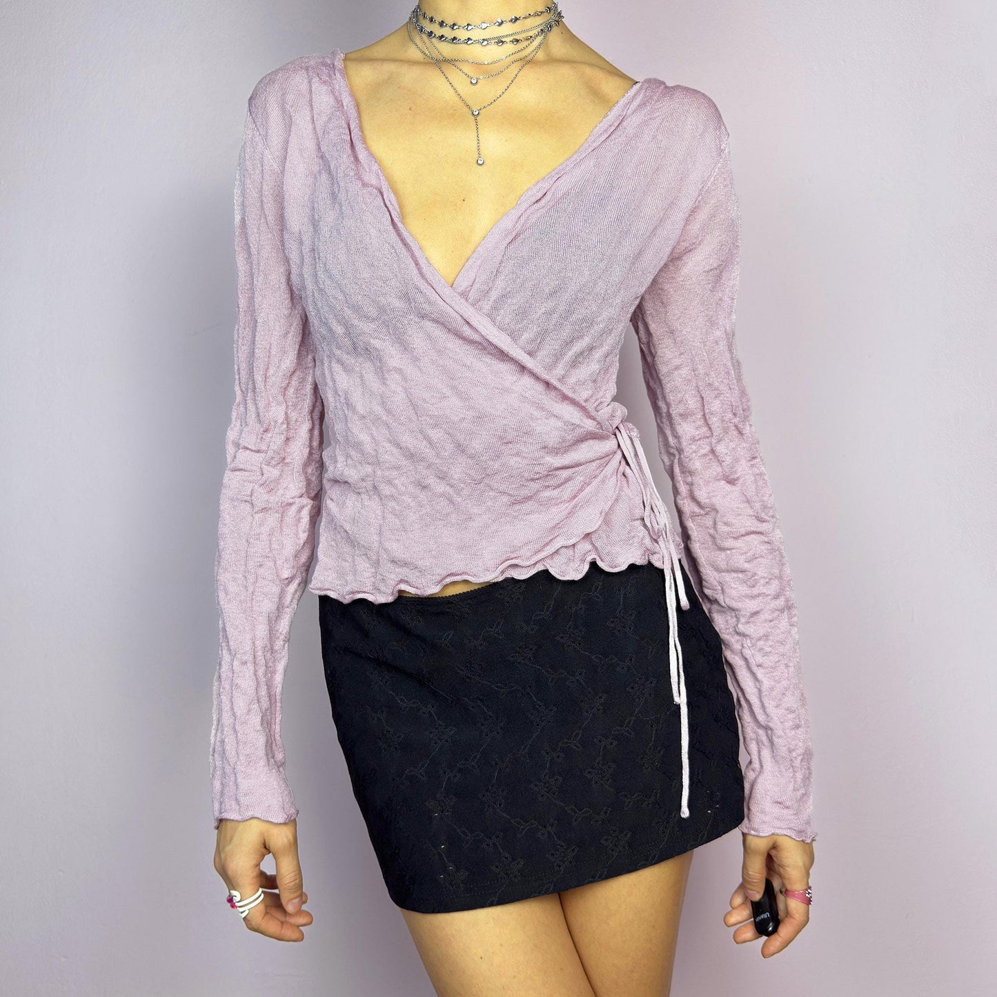 The Y2K Pink Wrap Tie Cardigan is a vintage 2000s delicate and feminine piece featuring a light pink hue and a textured knit fabric. Its wrap-around design ties at the side, creating an adjustable and flattering fit. adult world shop