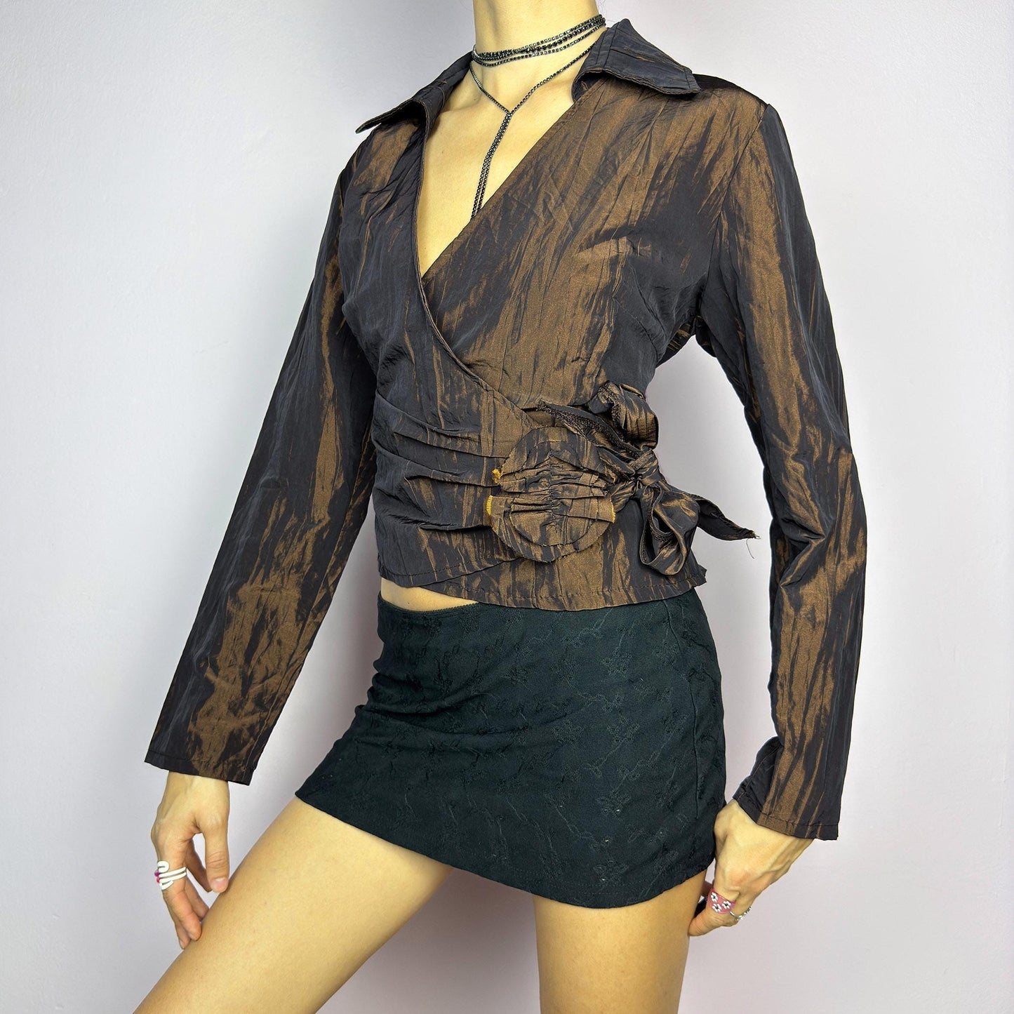 The Vintage 90s Brown Wrap Tie Blouse features a textured, crinkled fabric with a subtle iridescent finish, a flattering wrap design with a tie at the side. The deep brown tone adds versatility, while the structured collar. adult world shop