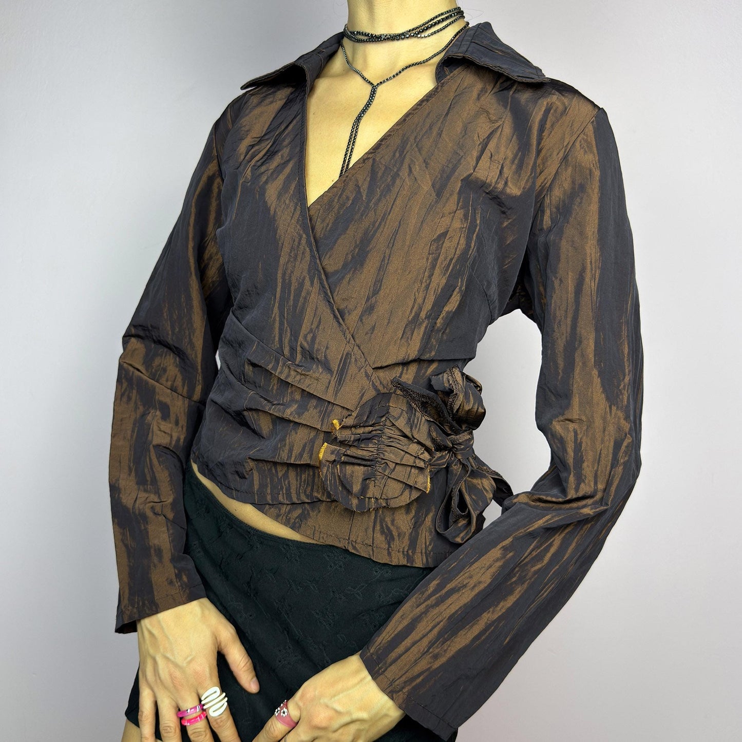 The Vintage 90s Brown Wrap Tie Blouse features a textured, crinkled fabric with a subtle iridescent finish, a flattering wrap design with a tie at the side. The deep brown tone adds versatility, while the structured collar. adult world shop