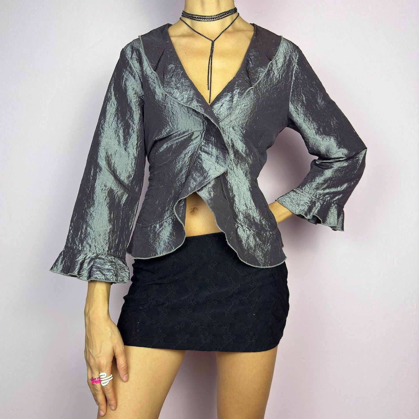The Vintage 90s Gray Iridescent Ruffle Blouse is a sophisticated and elegant piece with a shimmering iridescent finish in a metallic gray tone. It features a crinkled texture, a cascading ruffle trims along the hemline. adult world shop
