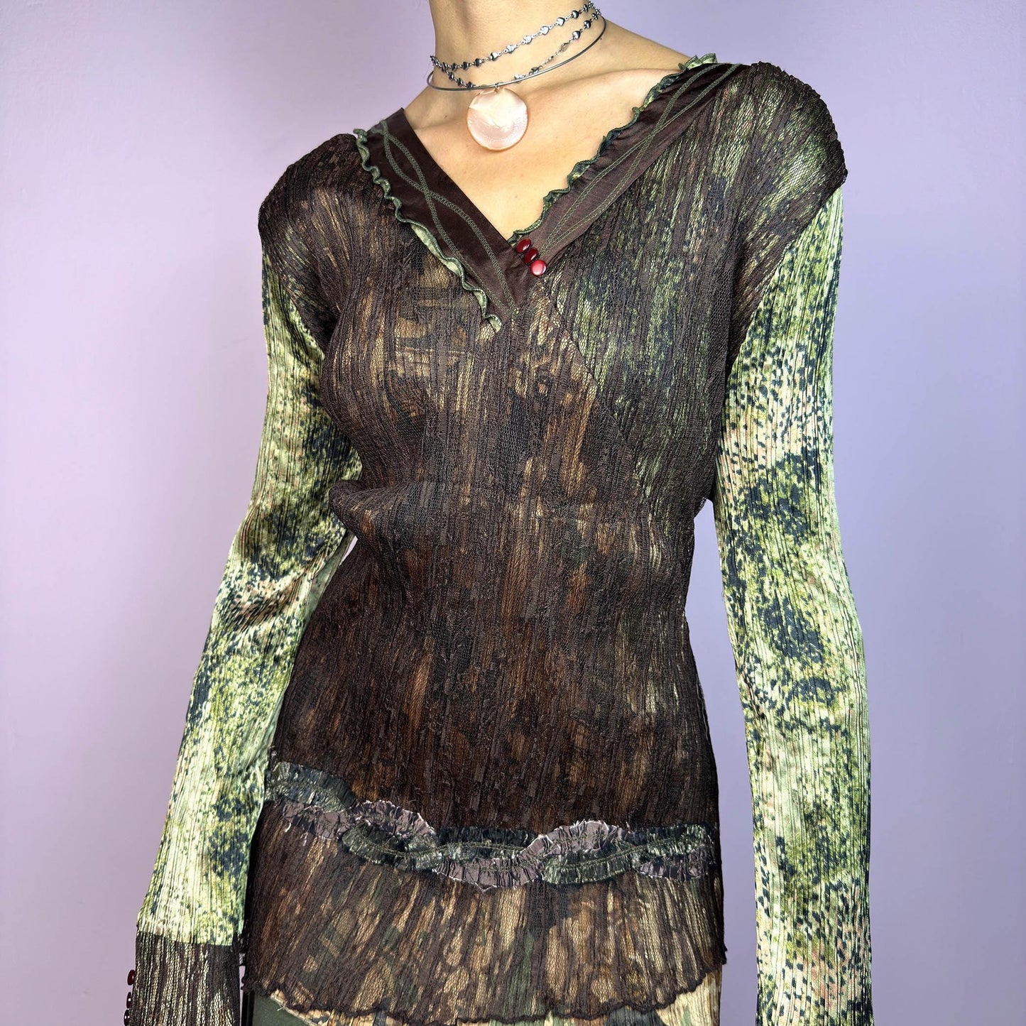 The Y2K Lace Asymmetric Layered Top is a vintage 2000s piece featuring an earthy mix of brown and green tones with a textured, stretchy fabric. This unique top showcases a V-neckline adorned with delicate lace trim, button details. adult world shop