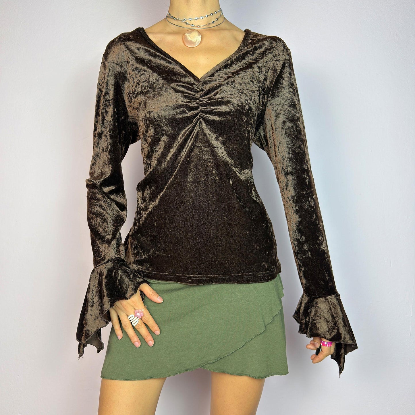 The Vintage 90s Brown Velvet Top is an elegant piece crafted from soft, stretchy velvet fabric. It features a rich chocolate brown hue, a flattering V-neckline with ruching detail at the bust, and dramatic bell sleeves. adult world shop