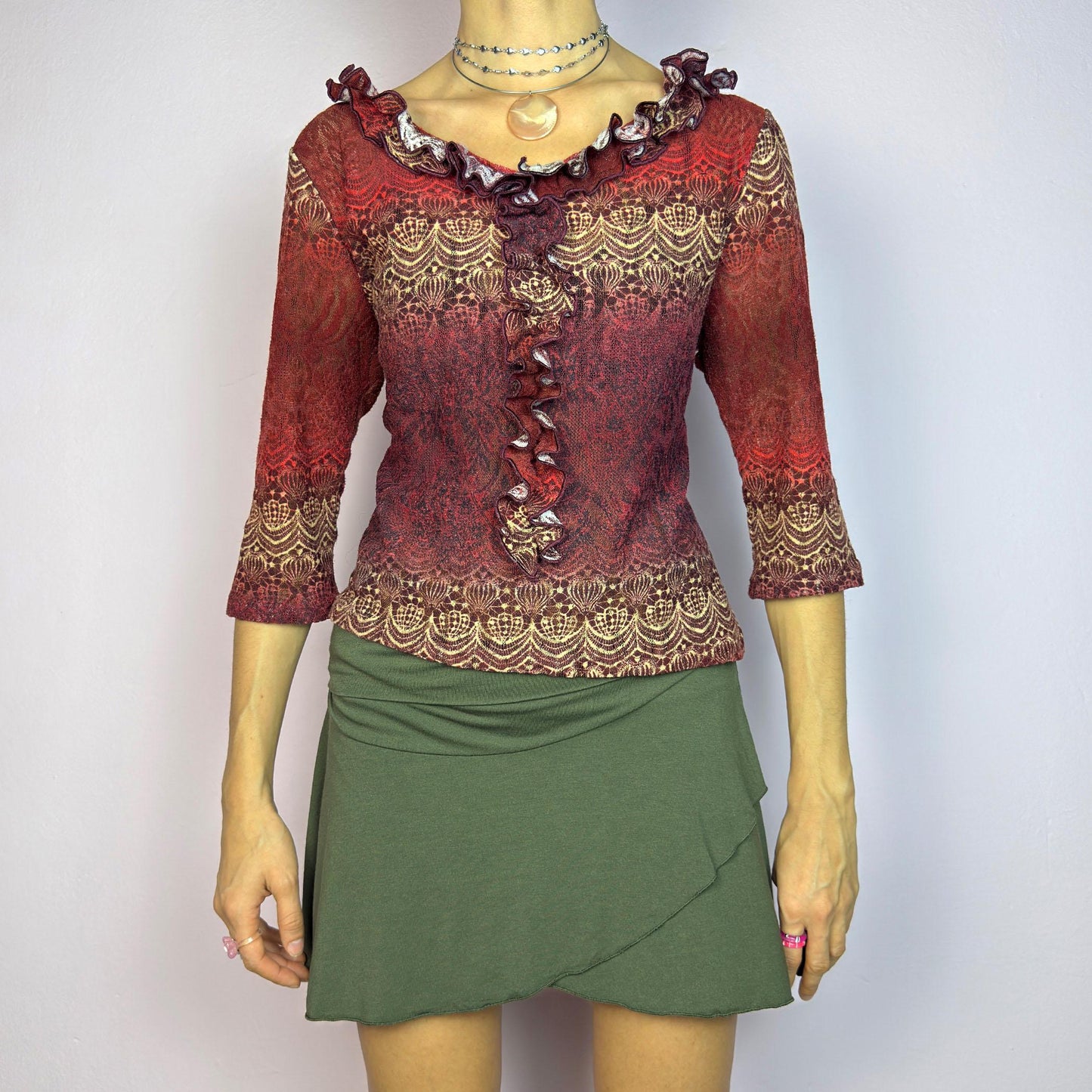 The Y2K Maroon Ruffle Mesh Top is a romantic vintage 2000s piece. Featuring a semi-sheer lace-inspired design in warm red tones, it showcases intricate patterns complemented by a ruffled neckline and 3/4 sleeves. adult world shop