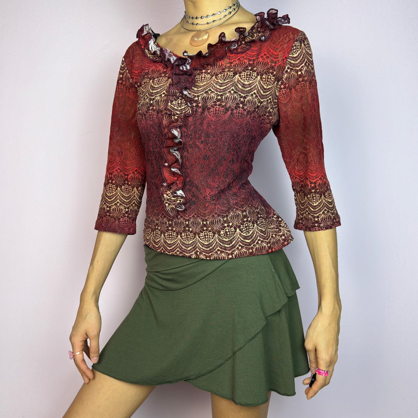 The Y2K Maroon Ruffle Mesh Top is a romantic vintage 2000s piece. Featuring a semi-sheer lace-inspired design in warm red tones, it showcases intricate patterns complemented by a ruffled neckline and 3/4 sleeves. adult world shop