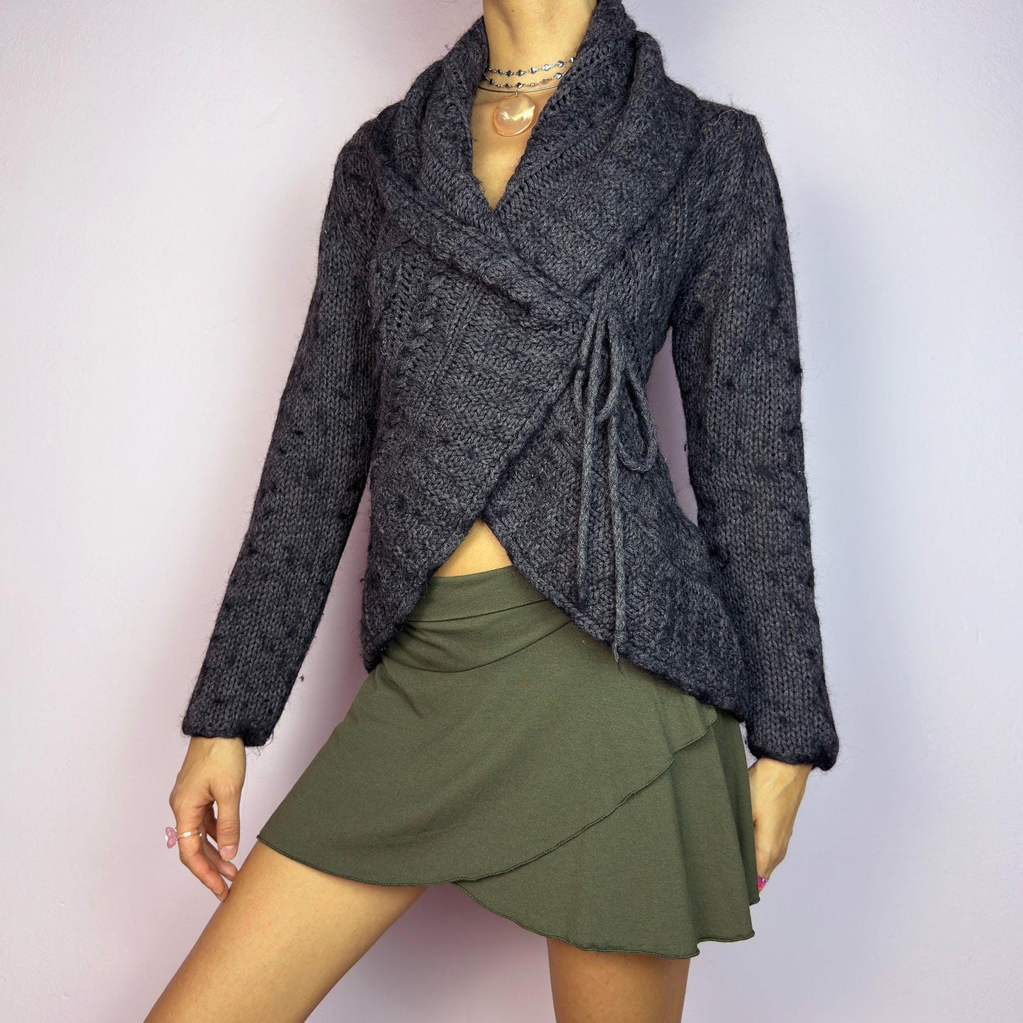 The Y2K Gray Wrap Tie Cardigan is a cozy vintage 2000s piece. This dark gray cardigan features a chunky knit design with intricate cable-knit detailing and a wrap-front closure that ties at the side for an adjustable fit. adult world shop