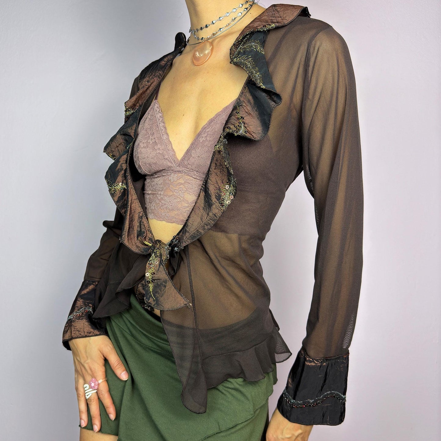 The Y2K Brown Mesh Tie Front Top is a vintage 2000s elegant and flirty piece. This semi-sheer mesh blouse features a tie-front closure and a cascade of ruffle detailing along the neckline and cuffs. adult world shop