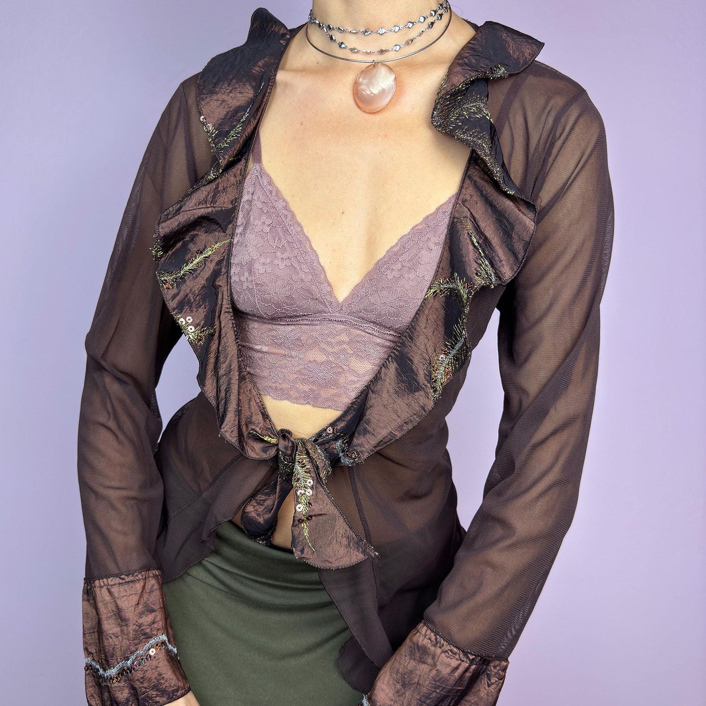 The Y2K Brown Mesh Tie Front Top is a vintage 2000s elegant and flirty piece. This semi-sheer mesh blouse features a tie-front closure and a cascade of ruffle detailing along the neckline and cuffs. adult world shop