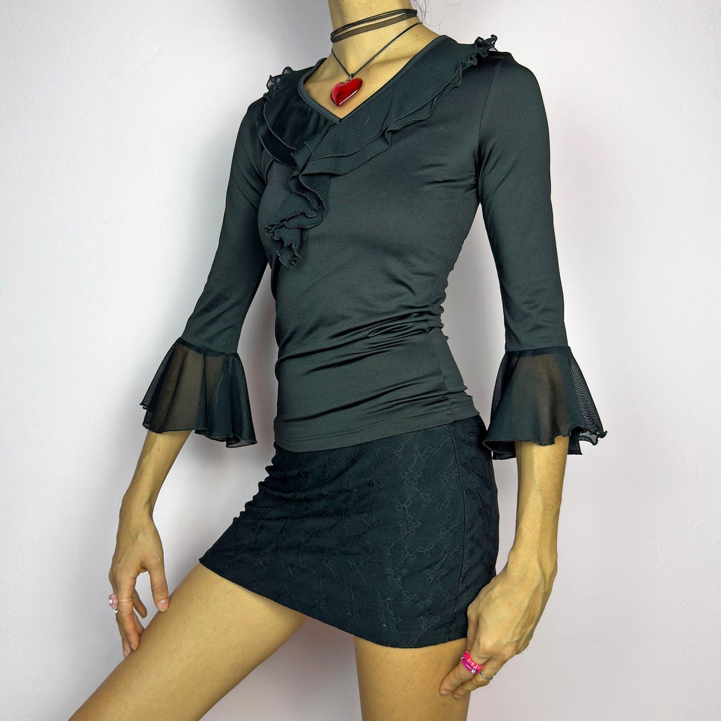 The Y2K Black Ruffle Bell Sleeve Top is a sleek and elegant vintage 2000s piece. Featuring a fitted silhouette with cascading ruffles along the neckline and a flattering V-neck design. The three-quarter bell sleeves with sheer mesh. adult world shop