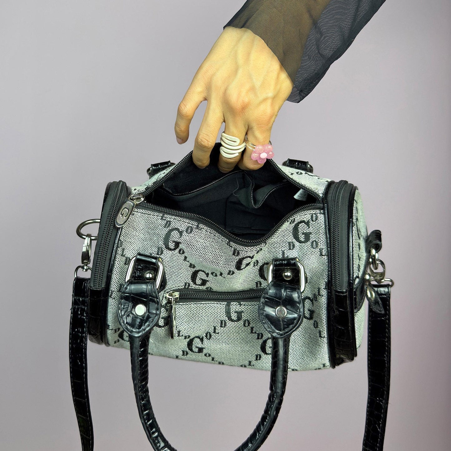 The Y2K Monogram Mini Duffel Bag is a stylish vintage 2000s accessory. Featuring a structured silhouette with an all-over monogram print, sleek black faux patent leather accents, and silver hardware. It includes dual top handles. adult world shop