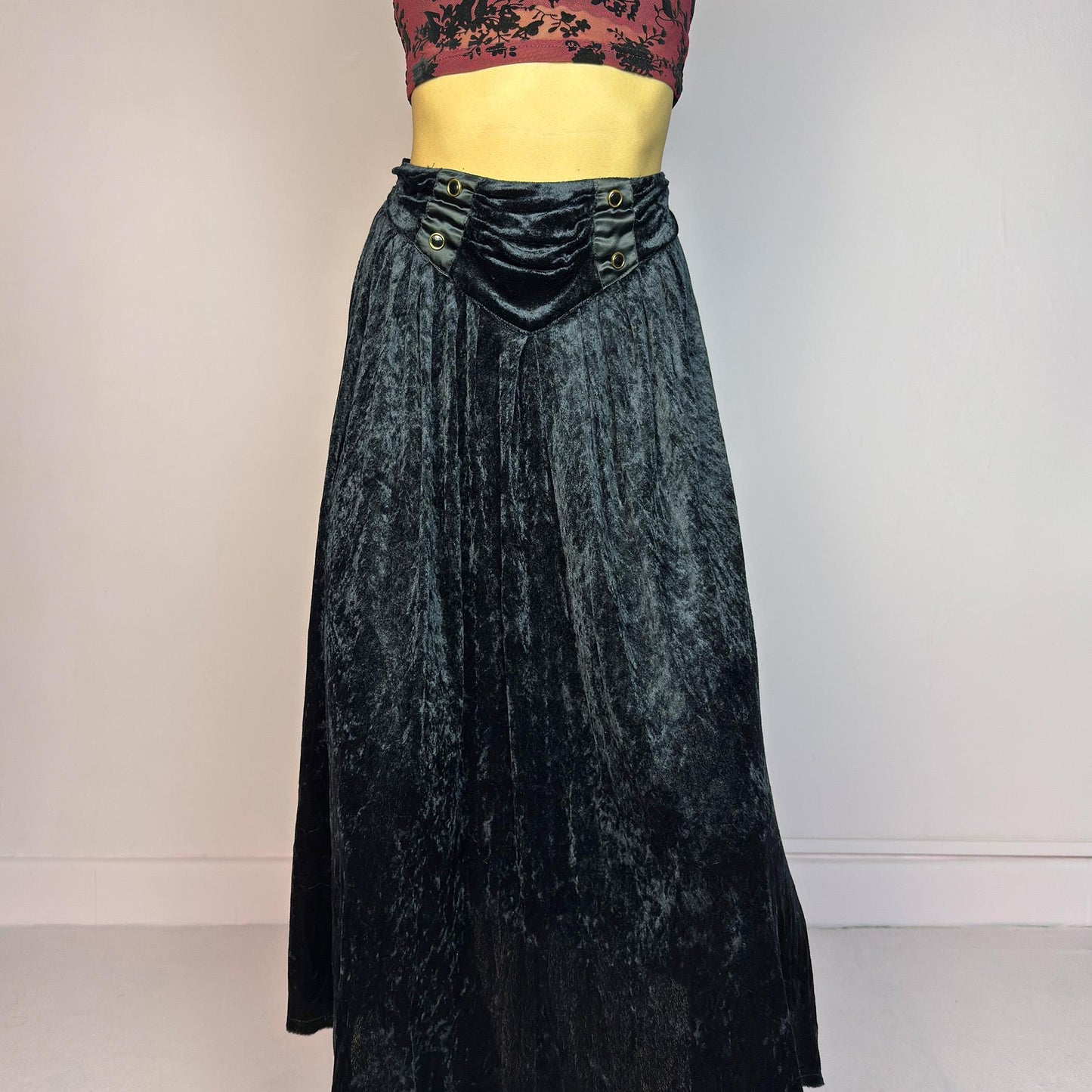 The Vintage 90s Black Velvet Midi Skirt is crafted from soft velvet and features an elastic waistband detail with button accents and a flowing A-line silhouette. Ideal for night parties and embodies a whimsical goth aesthetic. Adult World Shop