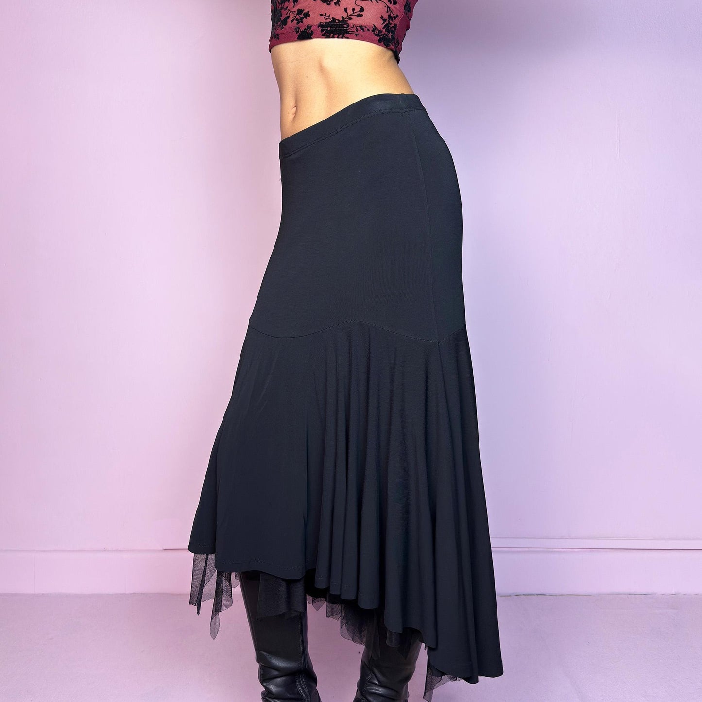 The Vintage 90s Layered Black Midi Skirt features a layered design with an asymmetrical hemline and a delicate tulle underlayer and an elastic waist. The trumpet silhouette enhances the figure, creating a dramatic and elegant flair. Adult World Shop